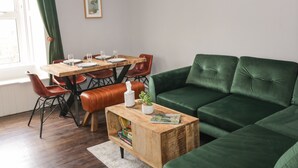 Et spiseområde med et træbord og røde stole, en grøn sofa og et lille træsofabord med en plante.