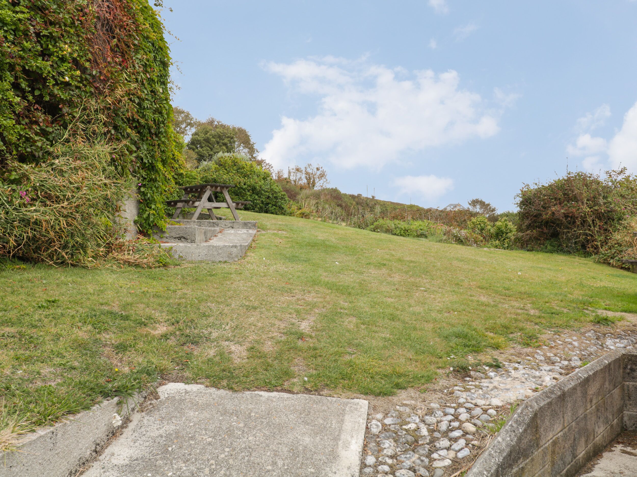 A grassy area with a concrete bench and steps leading up to a stone structure.