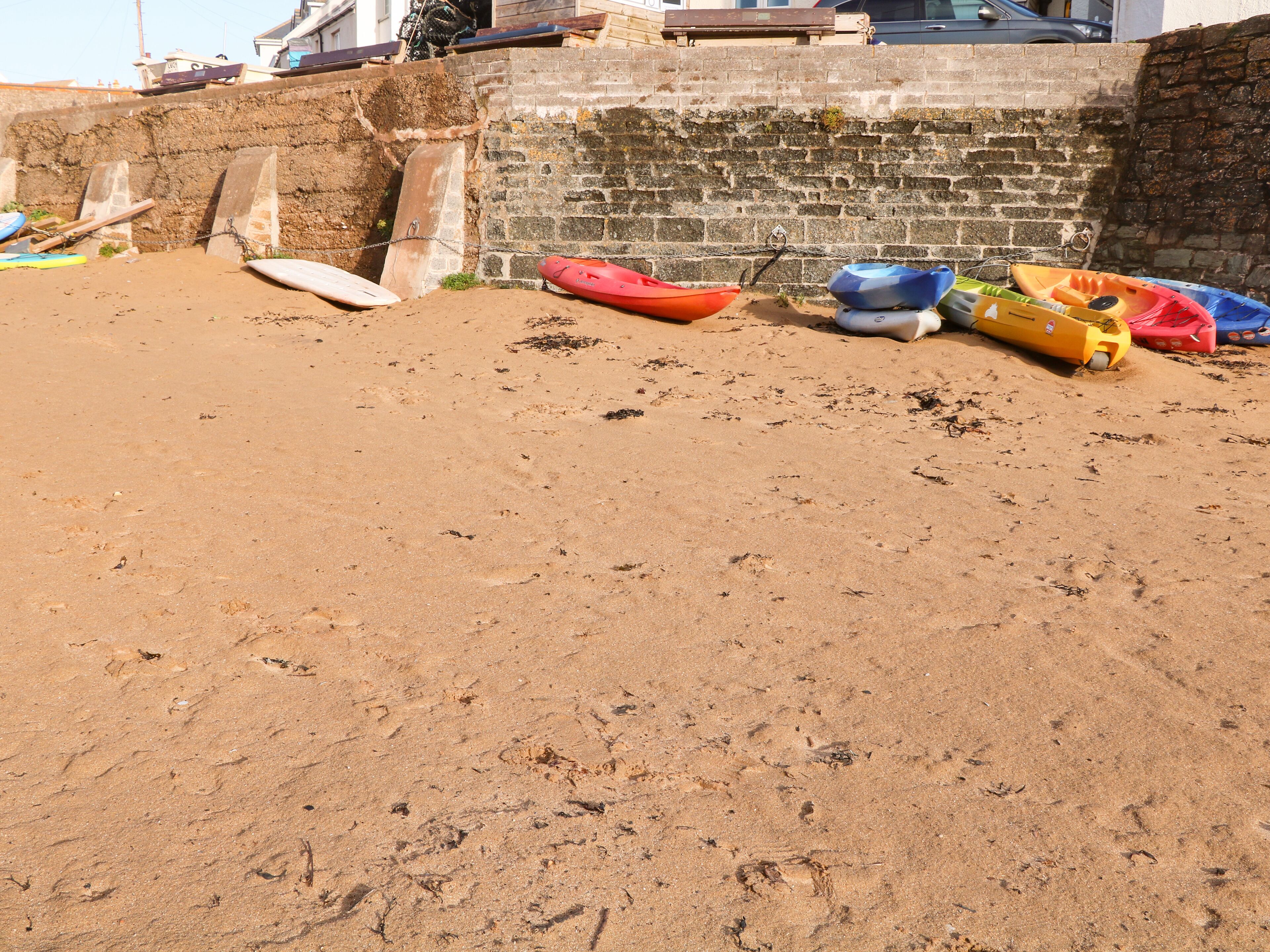 Een zandstrand met enkele kayaks en een surfplank.