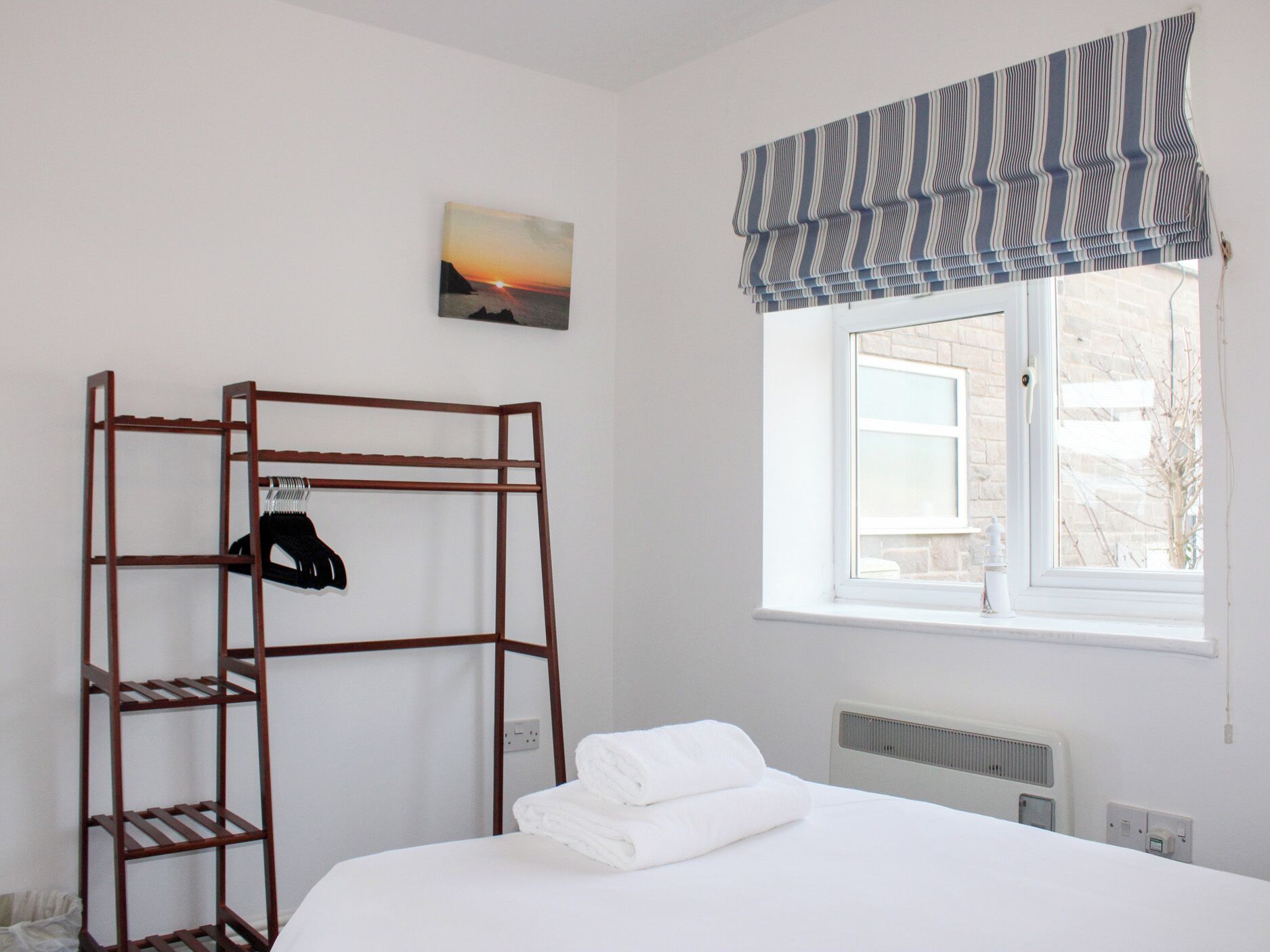 A bedroom with a bunk bed, a radiator, a window with a striped valance, and a painting of a sunset.
