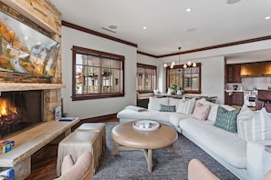 A modern living room with a fireplace, a large window, a sofa, and a kitchen area.
