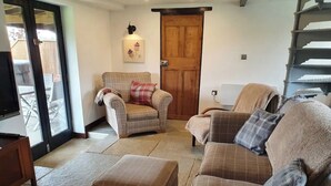 A living room with a sofa, armchair, ottoman, and a wooden door. - Bonneys Barn Retreat - Luxury homely getaway (000)