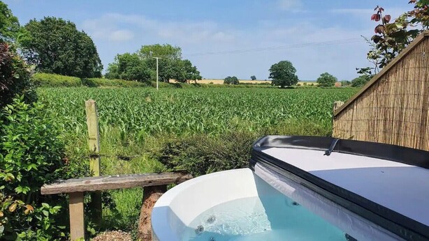 A hot tub in a garden with a view of a cornfield. - Bonneys Barn Retreat - Luxury homely getaway (000)