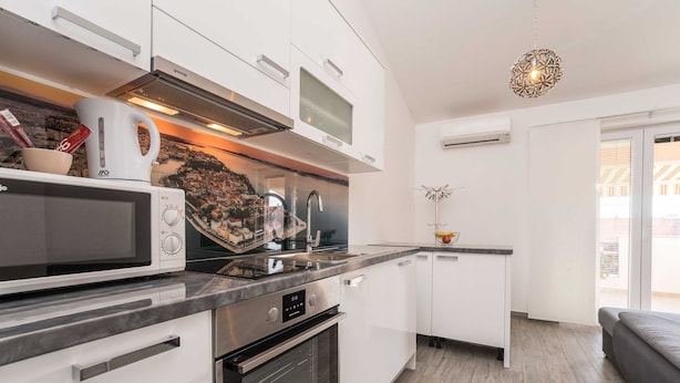 A modern kitchen with white cabinetry, a built-in microwave, a kettle, and a stainless steel range hood. - Apartments Maza (Zadar)