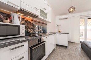 A modern kitchen with white cabinetry, a built-in microwave, a kettle, and a stainless steel range hood. - Apartments Maza (Zadar)