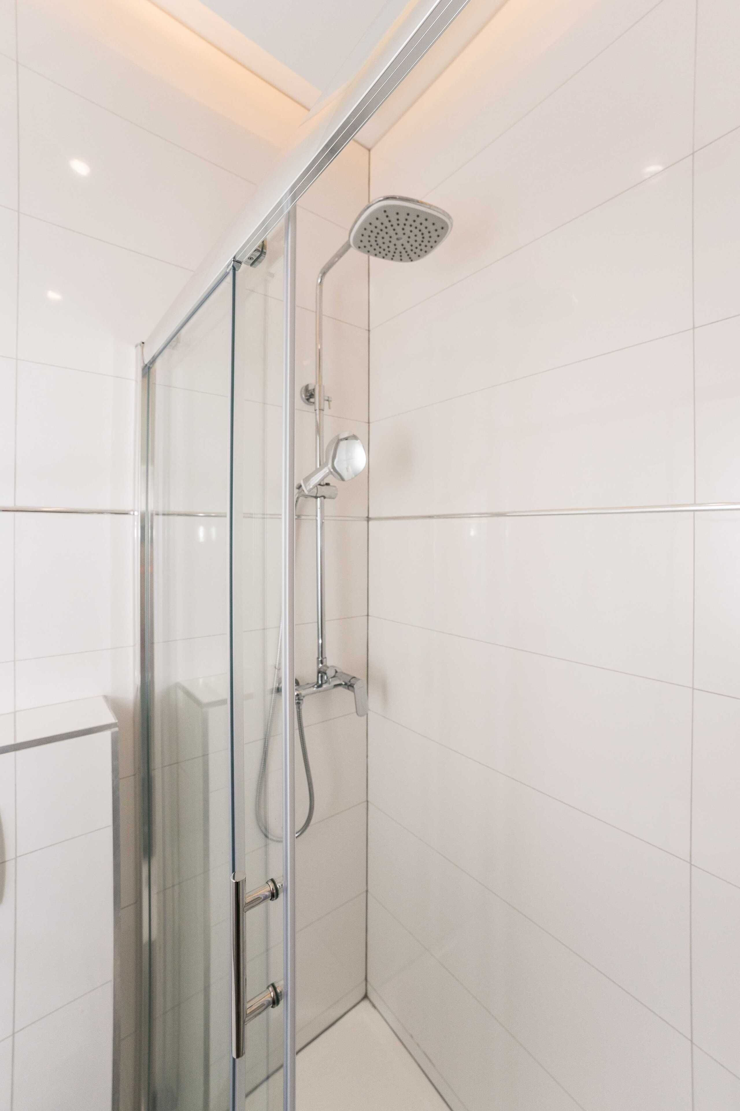 Una ducha moderna con mampara de vidrio, cabezal de ducha de mano y panel de control empotrado.