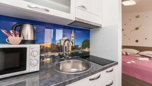 A modern kitchen with a stainless steel sink, a microwave, and a kettle. There is a decorative backsplash with a cityscape mural. - Apartments Maza (Zadar)