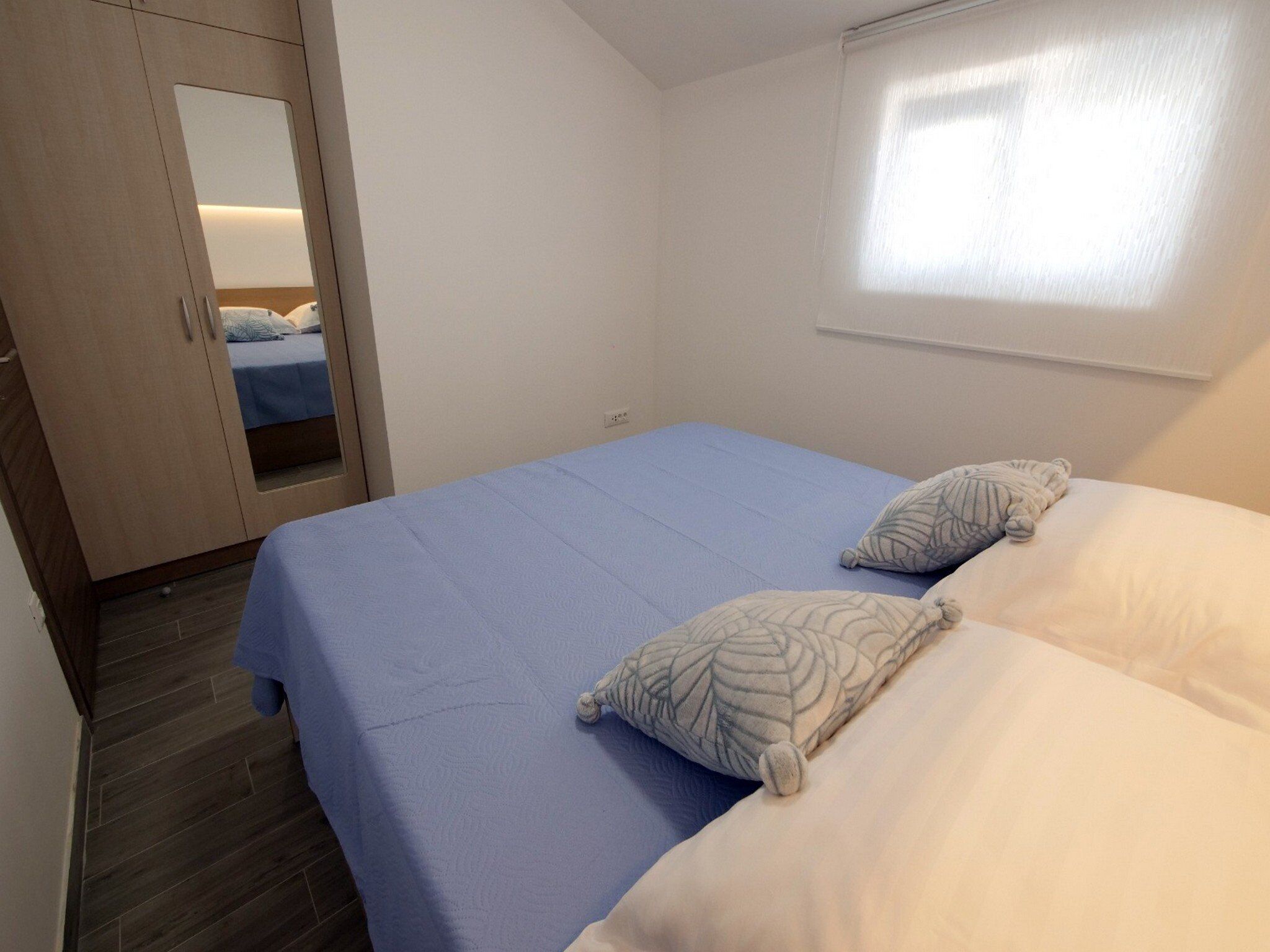 A bedroom with a bed, two pillows, a wardrobe, and a window.