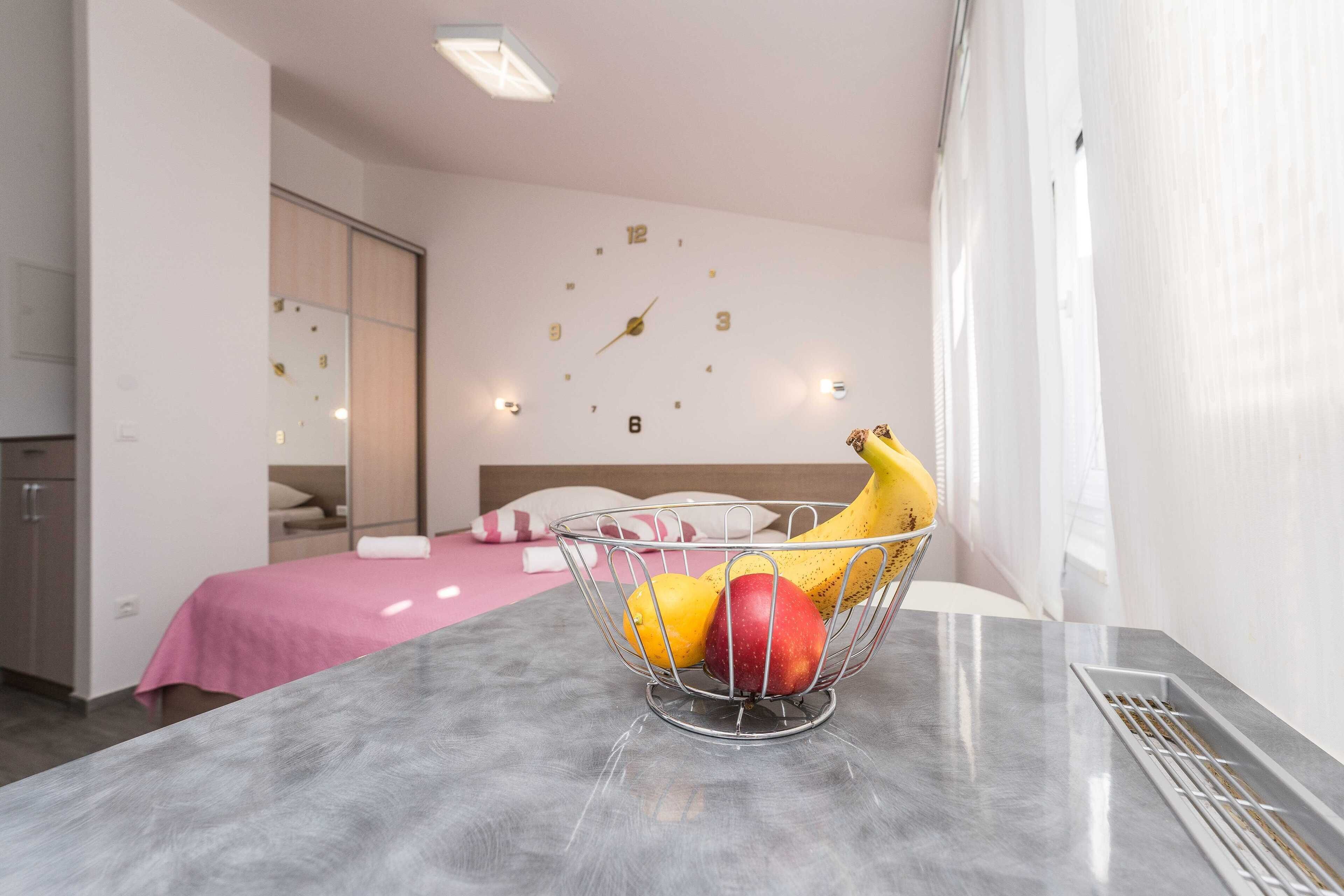 Een hotelkamer met een bed, een wandklok en een schaal fruit op een tafel.