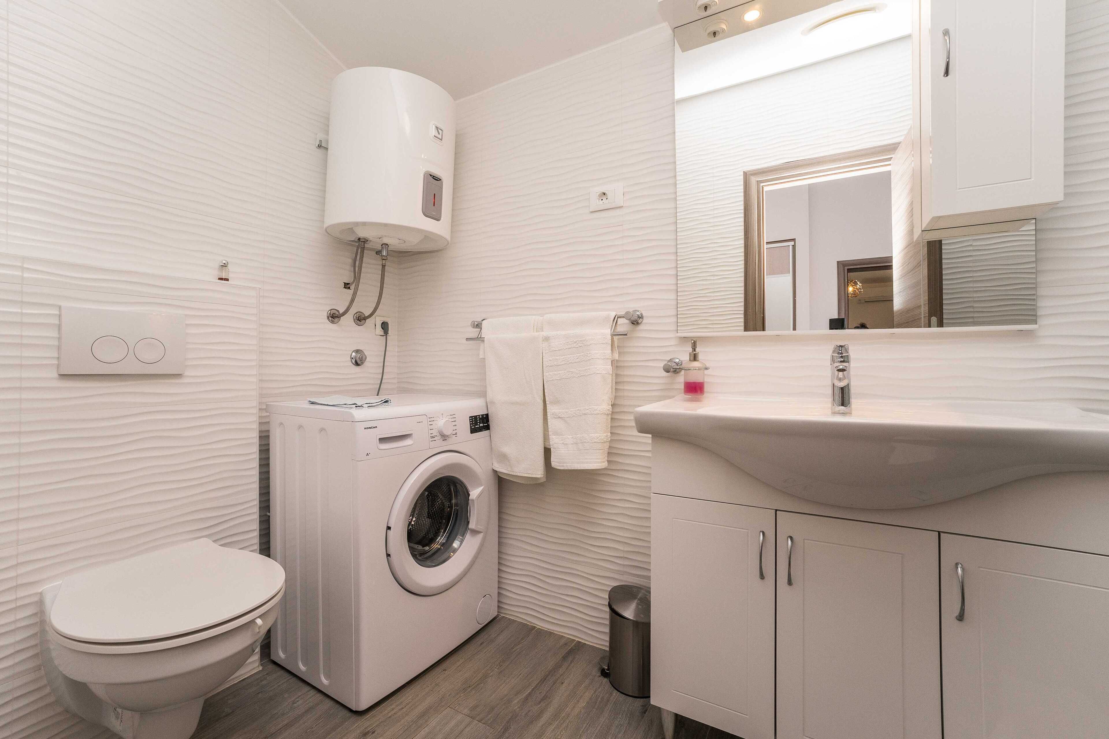 A modern bathroom with a washing machine, toilet, sink, and mirror.