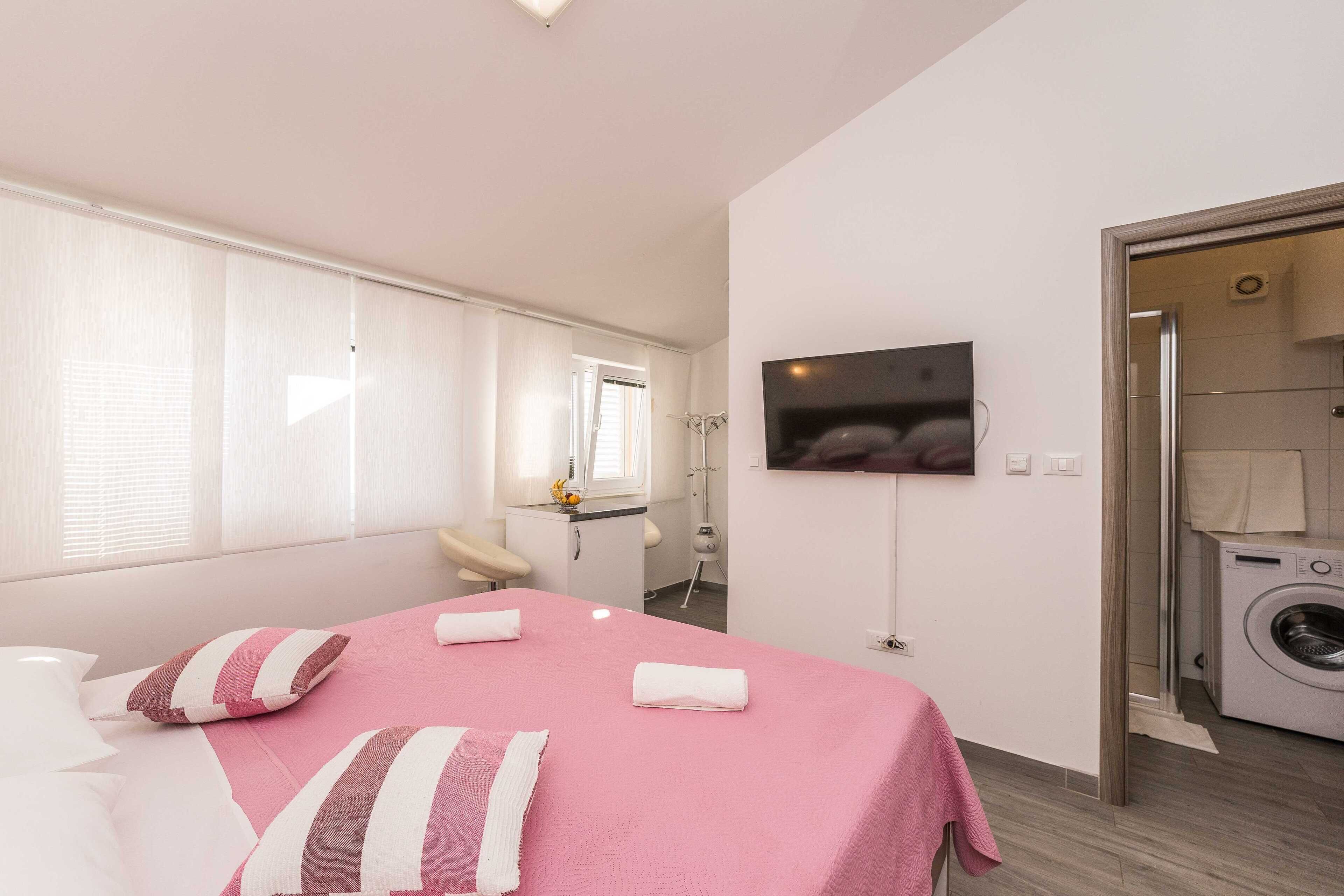 Habitación de hotel con cama, televisión, lavadora y baño visible a través de una puerta abierta.