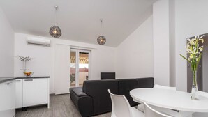 A modern living room with a black sofa, white chairs, a white table, and a vase of flowers. - Apartments Maza (Zadar)
