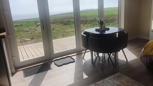 Une pièce dotée d’une porte-fenêtre coulissante donnant sur une terrasse, d’une table ronde avec des chaises, et offrant une vue sur un paysage verdoyant.