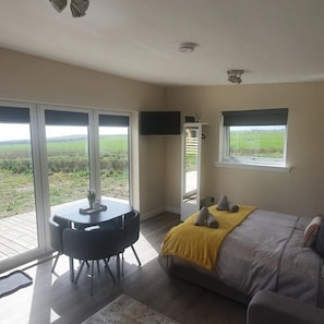 Une chambre à coucher avec un lit, une table et une chaise. Il y a une fenêtre donnant sur un champ.
