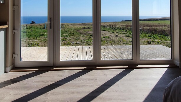 Une pièce dotée d’une grande porte-fenêtre coulissante qui donne sur une terrasse extérieure offrant une vue sur l’océan.