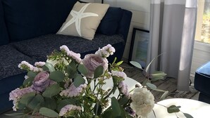 A living room with a dark blue sofa, a white cushion, a floor lamp, and a table with a vase of flowers.
