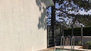 A clear swimming pool with a wooden deck edge, metal ladder, and a white wall in the background.