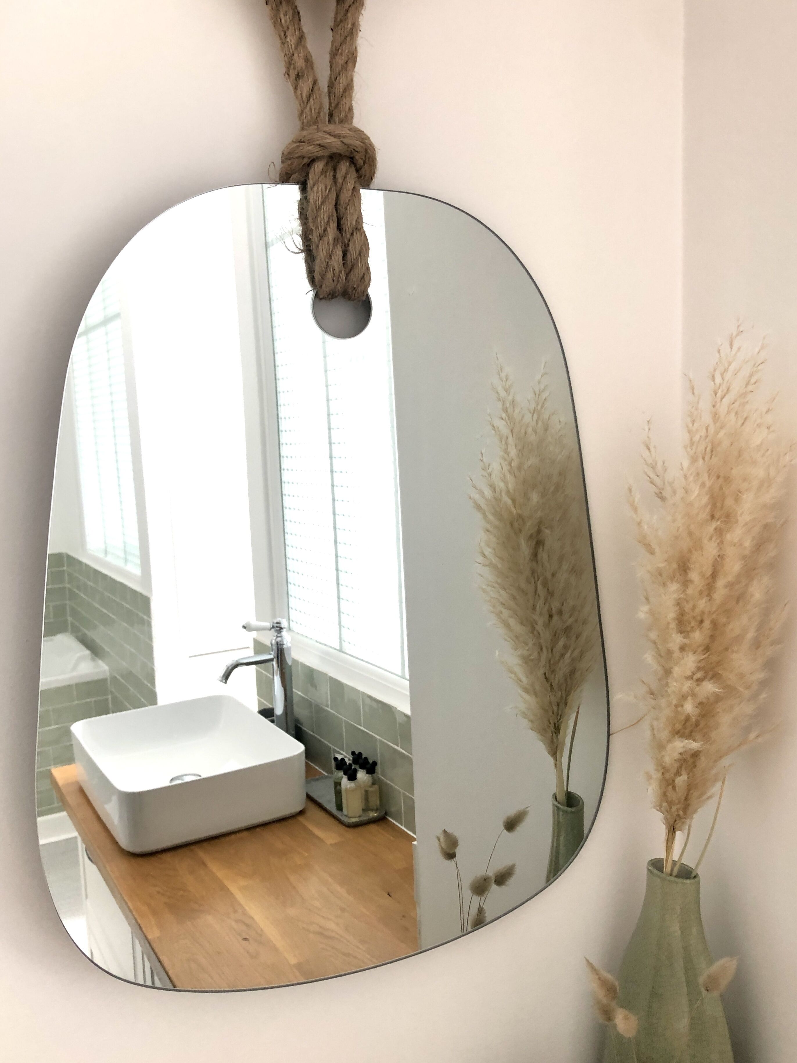 Une salle de bain avec un lavabo blanc, un miroir et des plumes d’herbe de la pampa dans un vase.