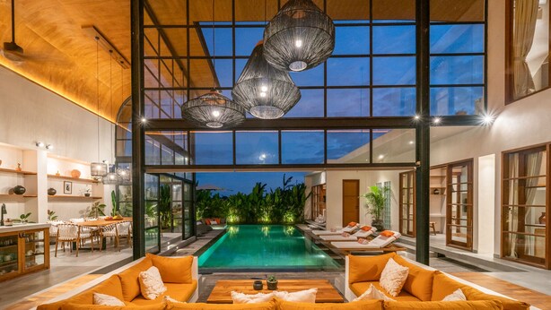 Un interior moderno con un amplio ventanal, una piscina y una zona de estar con sof ás naranjas.