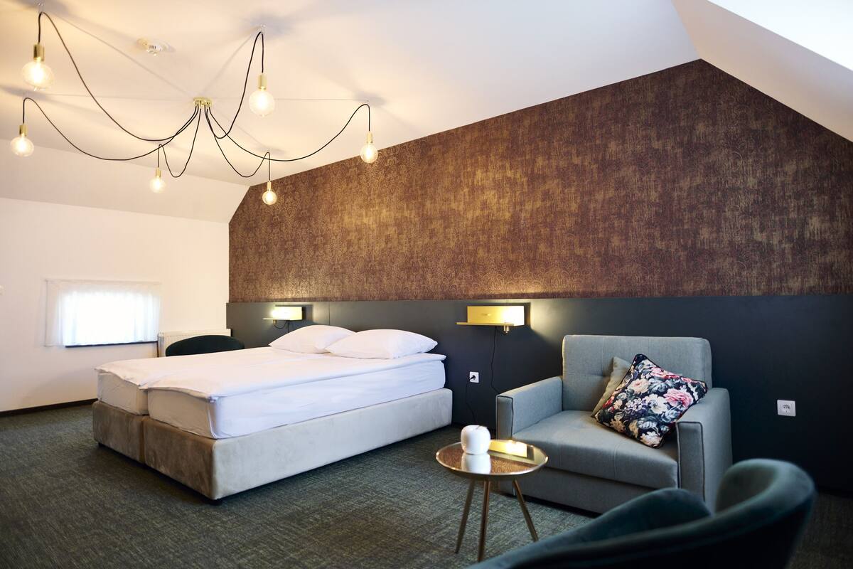 A modern hotel room with a bed, a sofa, a small round table, and a unique ceiling light fixture.