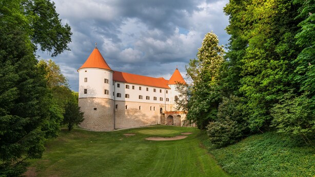 A castle with a red roof, surrounded by lush greenery and a well-maintained lawn. - Mokrice Castle Estate (Brezice)