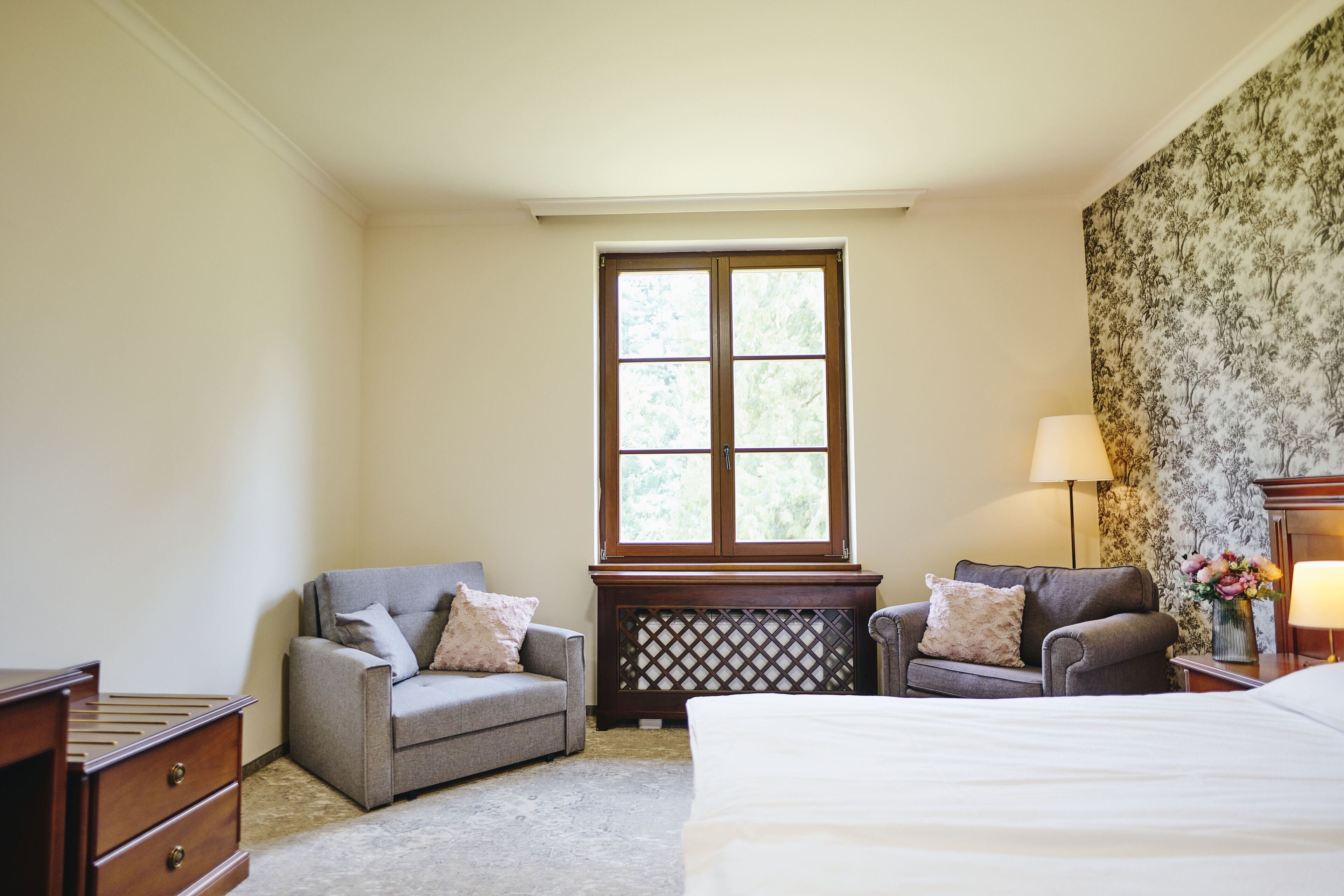 Une chambre à coucher avec un grand lit, deux fauteuils, une commode, une fenêtre et une lampe.