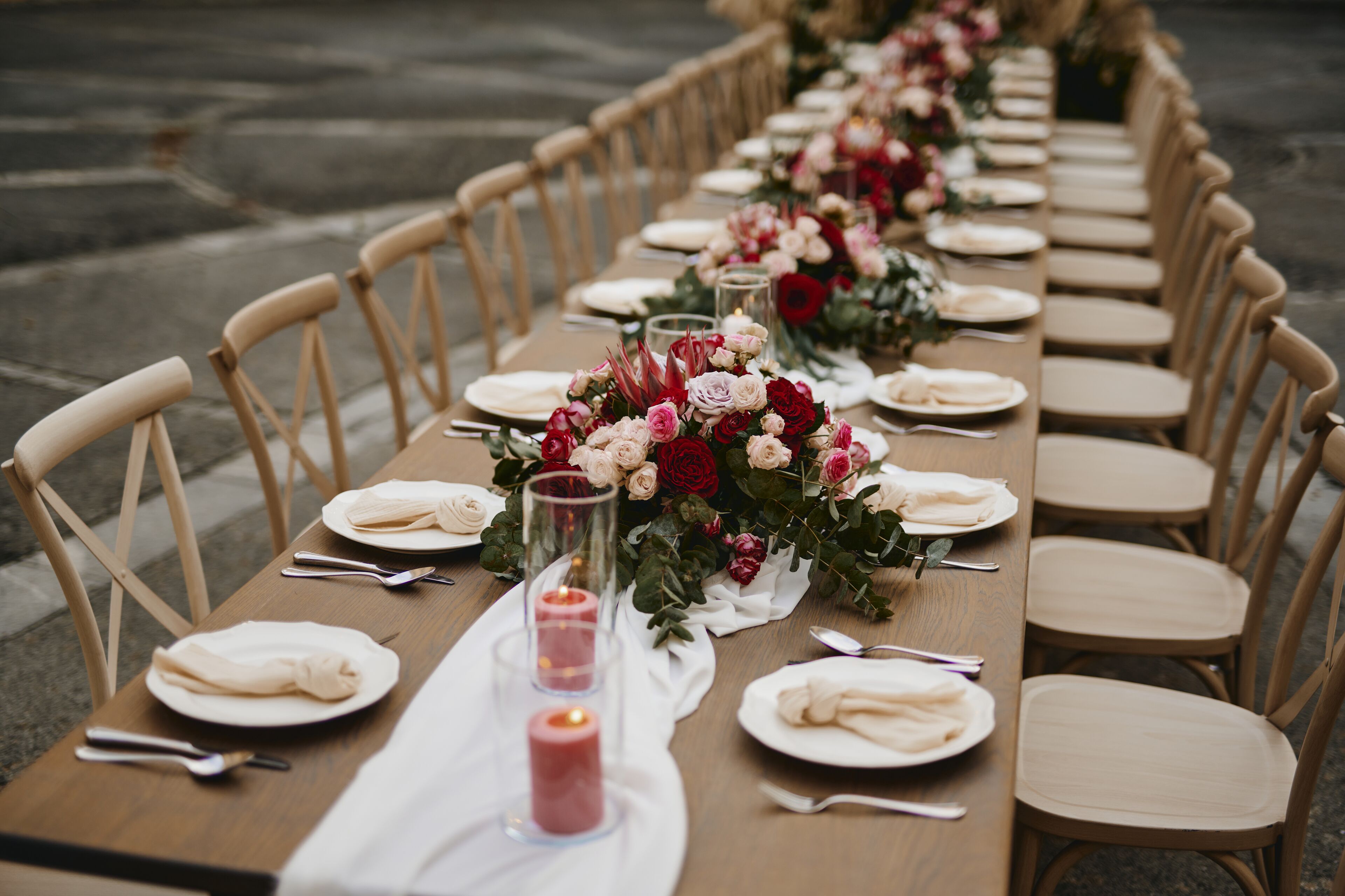 Una larga mesa de comedor dispuesta con sillas, platos, cubiertos y centros de mesa florales.
