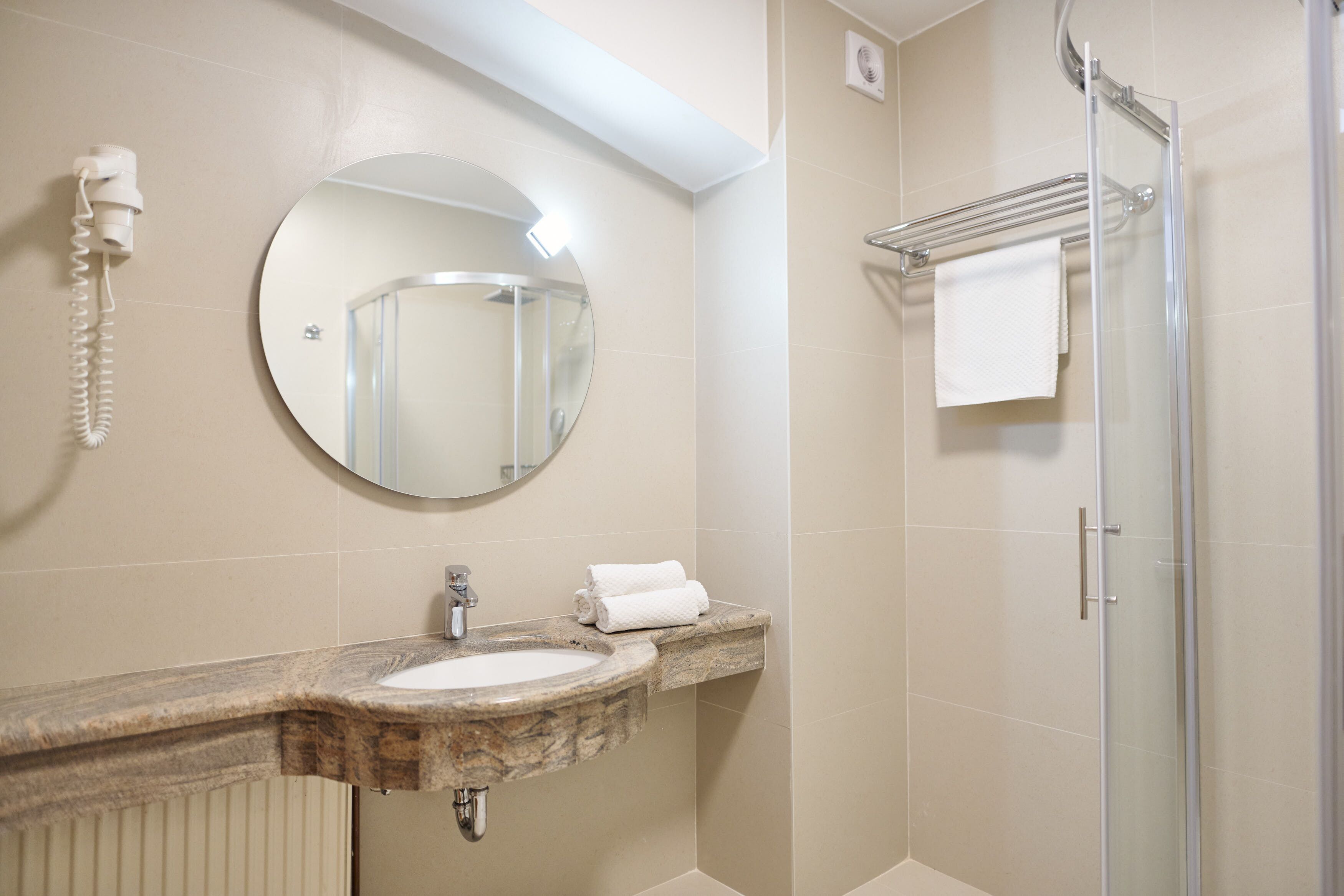 Une salle de bain avec un lavabo en marbre, un miroir rond, un porte-serviettes et une cabine de douche en verre.