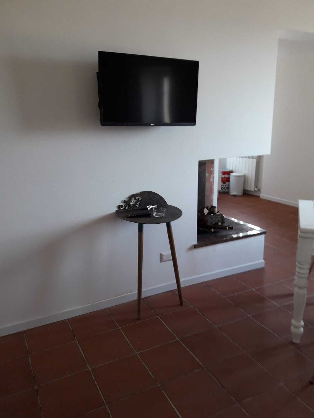 Une chambre dotée d’un téléviseur à écran plat fixé au mur, d’une petite table ronde avec une télécommande, et d’un radiateur recouvert d’une housse blanche.