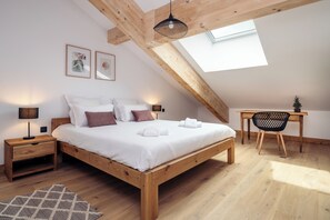Quarto com cama de madeira, mesas de cabeceira, escrivaninha e claraboia.