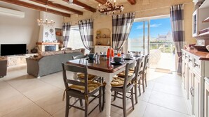 A spacious kitchen with a dining area, wooden beams, a chandelier, and a view of a castle. - Twilight Gozitan Farmhouse With Pool (Ghasri)