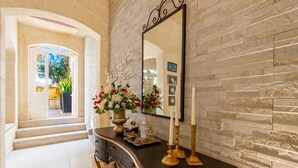 A hallway with a stone wall, a mirror, a dark wooden console table with a vase of flowers, and a staircase leading to another room. - Twilight Gozitan Farmhouse With Pool (Ghasri)