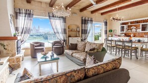 A spacious living area with a sofa, chairs, a dining table, and a kitchen area. - Twilight Gozitan Farmhouse With Pool (Ghasri)