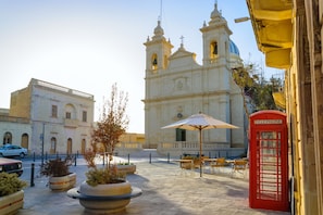 Une place avec une église, des tables et chaises à l’extérieur, et une cabine téléphonique rouge.