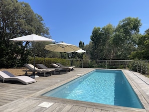 Relax by the pool surrounded by lush greenery and trees, with lounge chairs and umbrellas providing shade.