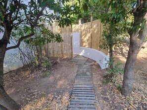 Stroll along the shaded pathway to a serene wooden deck surrounded by lush greenery and a bamboo fence.