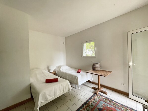 A small, clean room with two single beds, a small table with a woven basket, a window with a view of trees, and a sliding glass door. - Ruscana by Pinarello Villa Services (Pinarello)