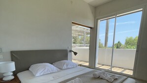 A bedroom with a large bed, a bedside table with a lamp, and a view of the outdoors through a sliding door. - Ruscana by Pinarello Villa Services (Pinarello)