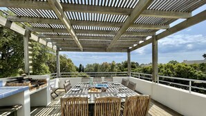 An outdoor patio with a wooden table and chairs, a grill, and a view of trees and hills. - Ruscana by Pinarello Villa Services (Pinarello)