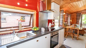 A compact kitchen with a sink, stove, and oven, a dining area with a table and chairs, and a window with a view of a building outside. - Robin's Nest (Keswick)
