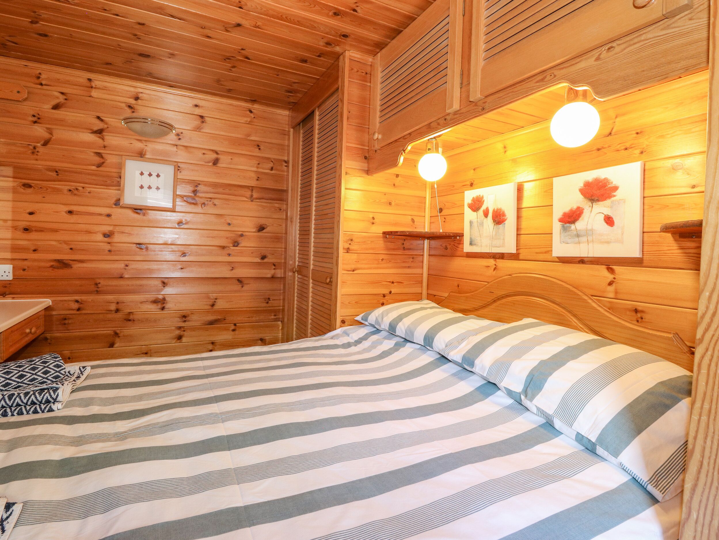 A wooden cabin room with a bed, a nightstand, and a wall-mounted shelf.