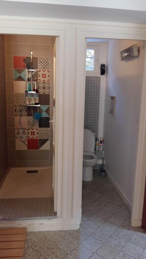 Un baño con zona de ducha con azulejos estampados, inodoro y lavabo.