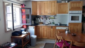 A compact kitchen with wooden cabinets, a built-in oven, and a window with curtains. - Apartment (Lège-Cap-Ferret)