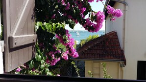 A view through a window with pink flowers, a tiled roof, and a body of water with boats in the distance. - Apartment (Lège-Cap-Ferret)