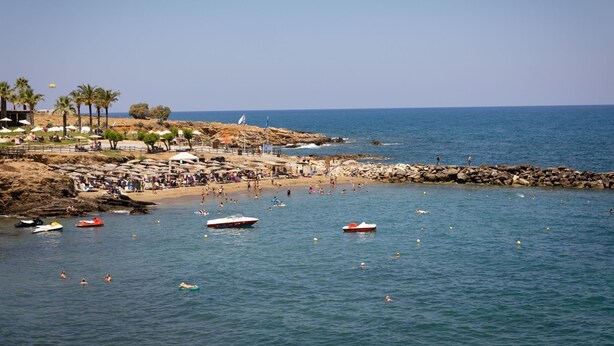 A beach with boats, people swimming, and a rocky shoreline.