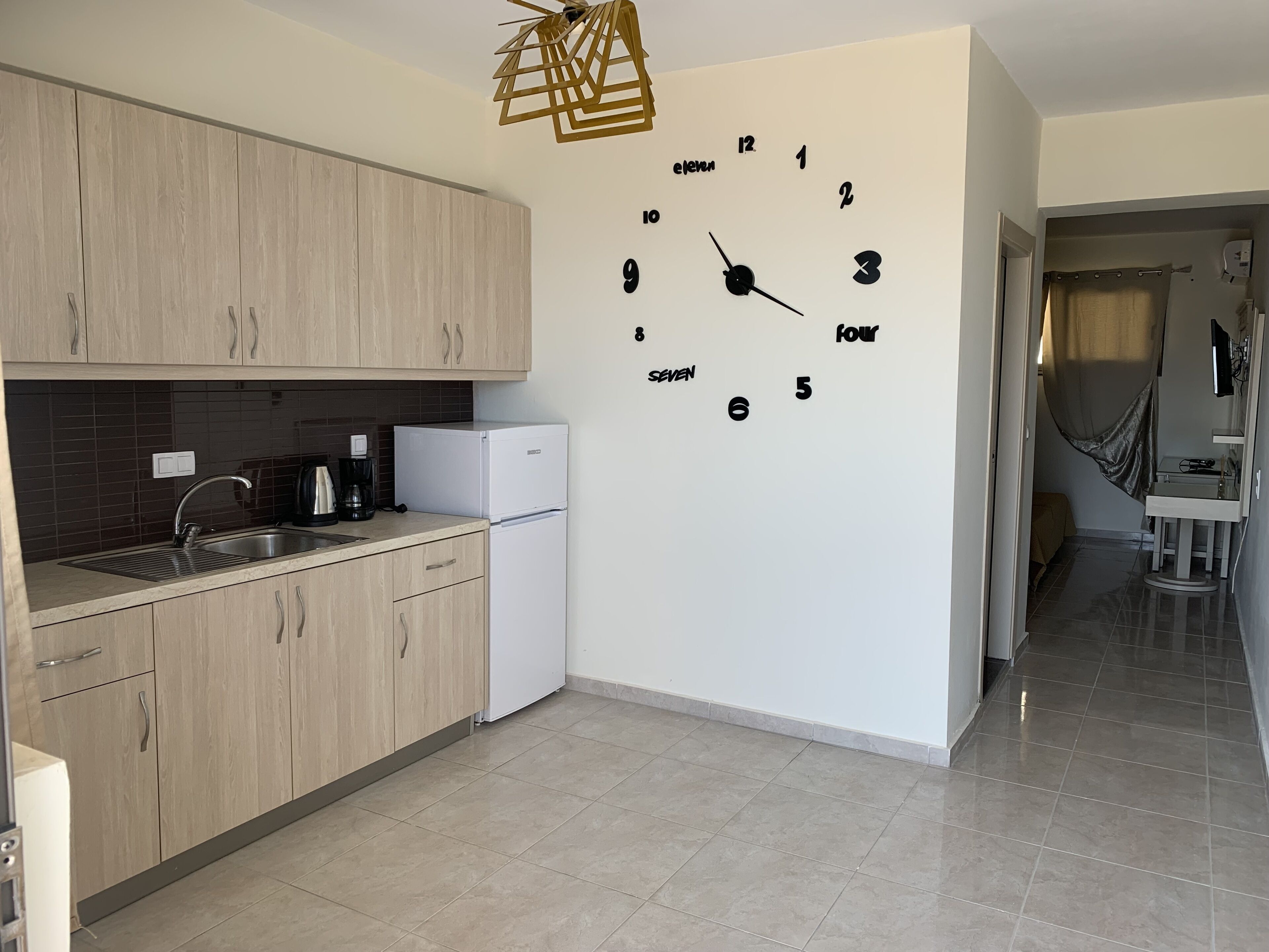 A modern kitchen with wooden cabinets, a white refrigerator, a built-in sink, and a wall clock.