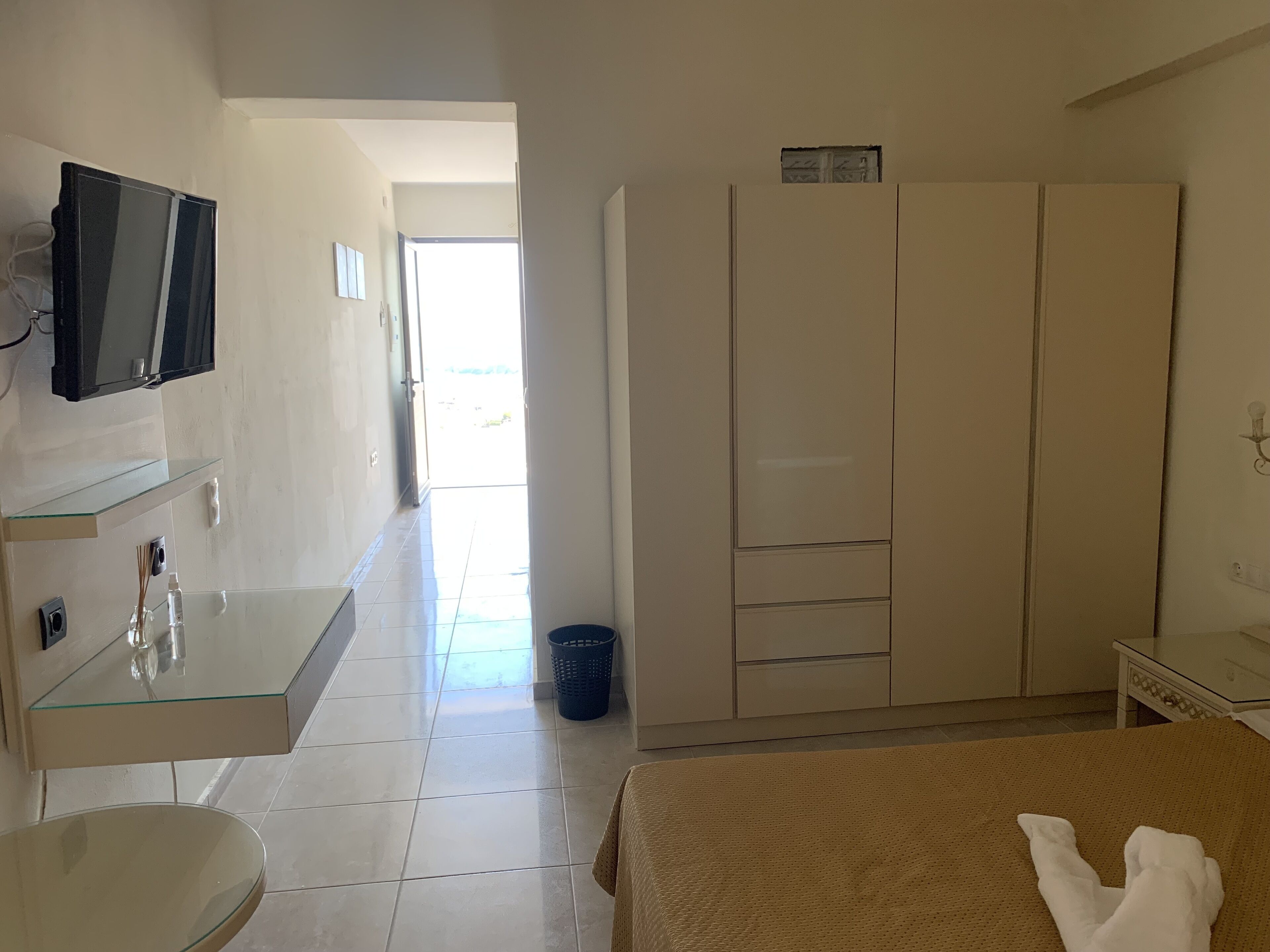 A hotel room with a bed, a TV mounted on the wall, a small desk with a mirror, and a wardrobe.