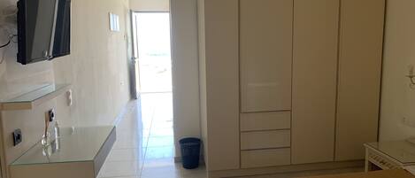 A hotel room with a bed, a TV mounted on the wall, a small desk with a mirror, and a wardrobe.
