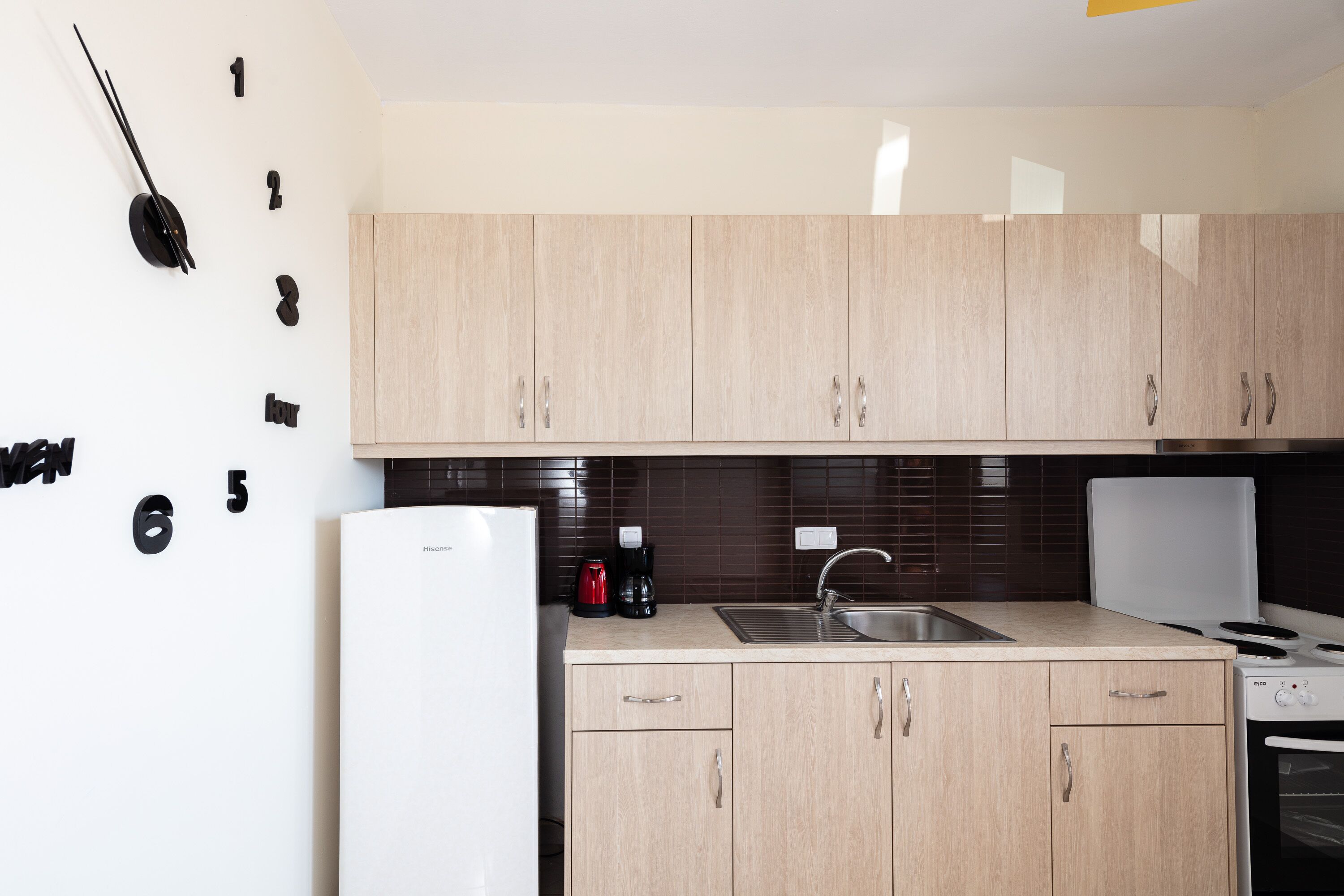 Una cocina moderna con armarios de madera clara, un refrigerador blanco, una cafetera y una estufa.