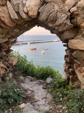 A stone archway leading to a rocky shoreline with boats on the water. - FabView Studio Apartments (Mylopotamos)
